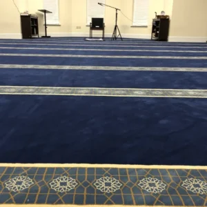Spacious prayer hall with blue carpet featuring intricate gold and white geometric patterns marking prayer rows